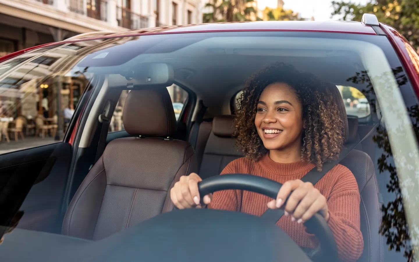 Motorista sorrindo ao volante do próprio carro, em uma rua da cidade.