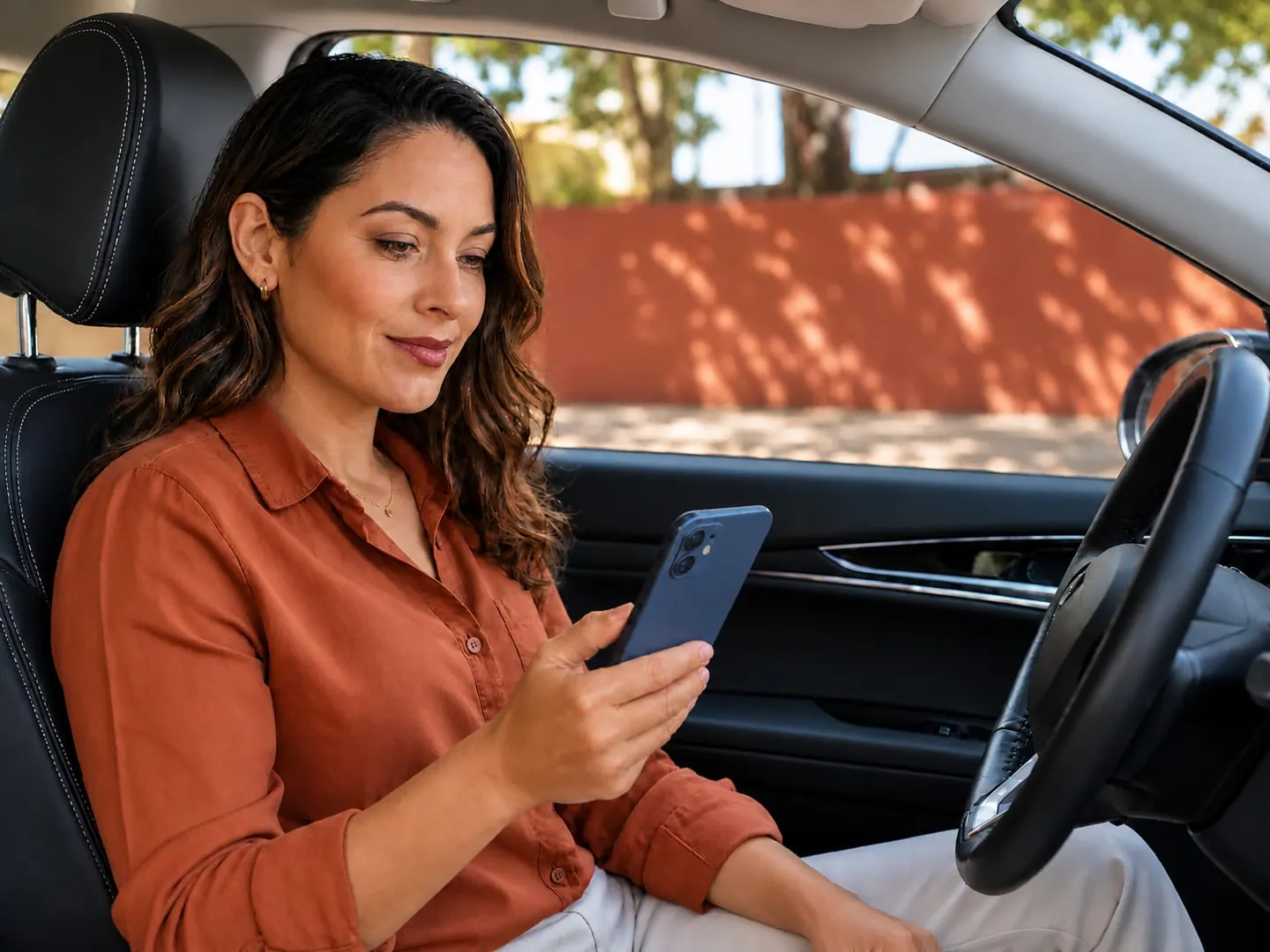 Mulher sentada no assento do motorista do próprio carro, fazendo uma simulação no celular.
